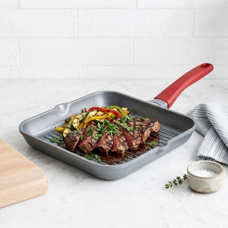 מחבת גריל 28 ס"מ TITANIUM FLAME ידית אדומה | Surround the cookware with light, airy styling props in the same clean, minimal, natural-light mood as "Visual Reference 1" — choose 1-2 simple elements such as